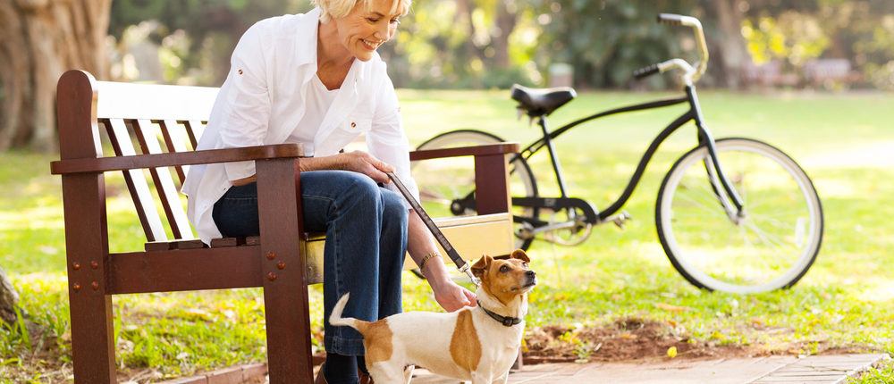 Woman who does peritoneal dialysis sitting on park bench smiling holding dog on leash